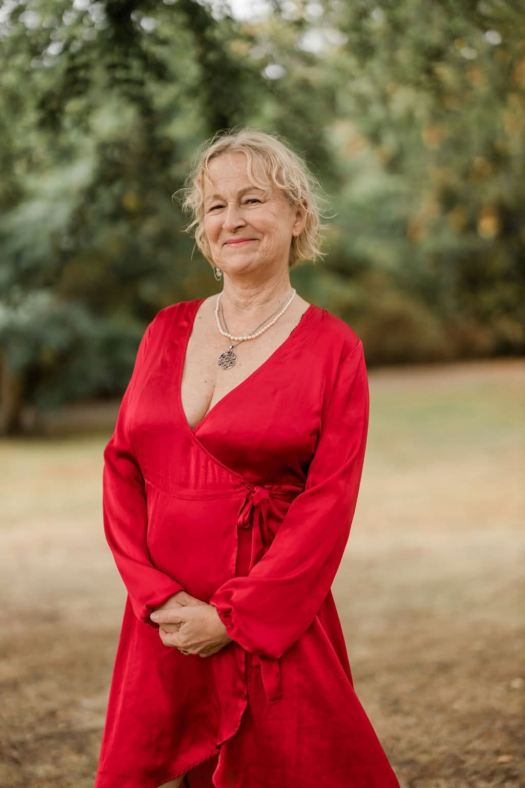 Kristina in a red dress with her hands gently clasped, smiling softly