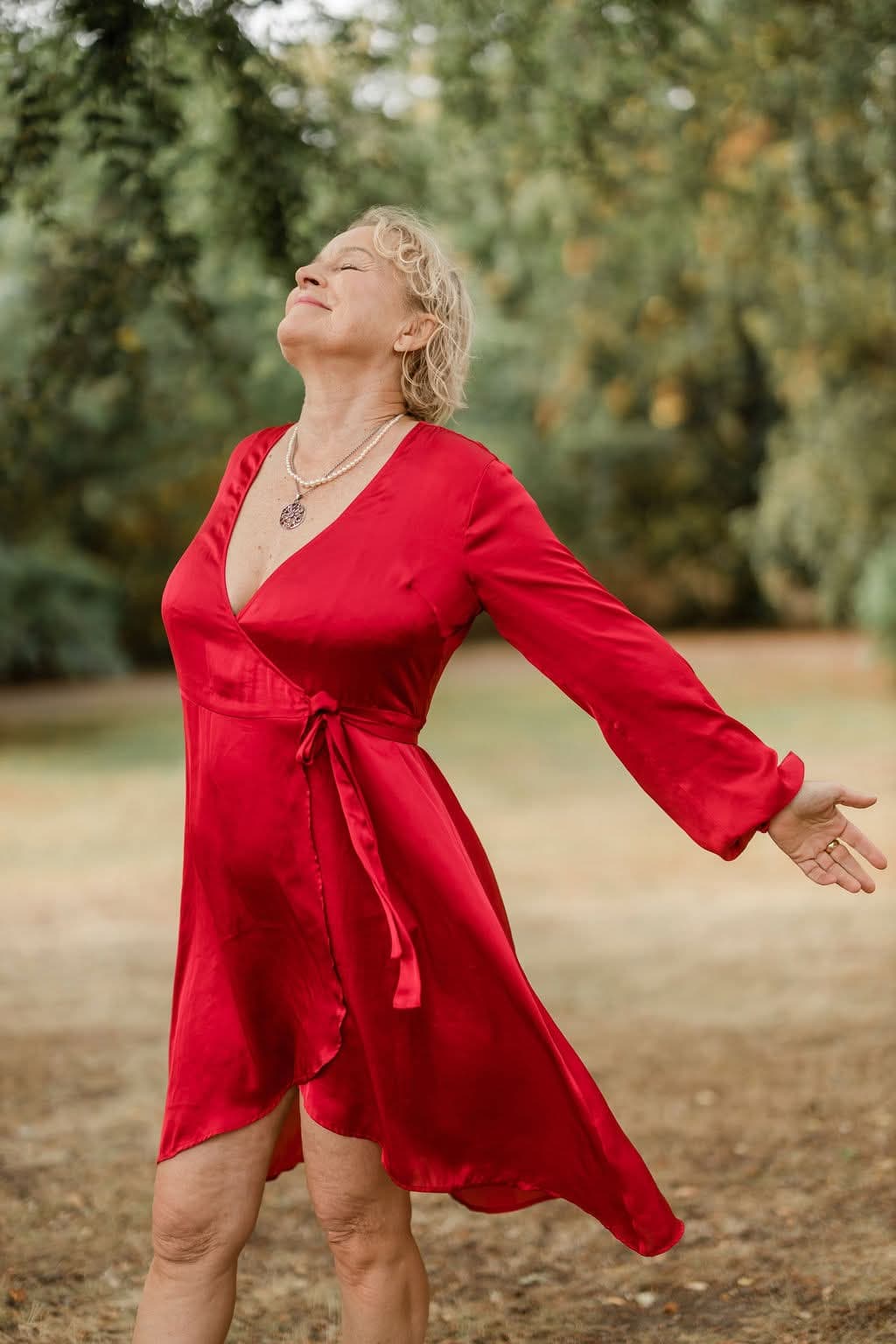 Kristina in a red dress with her arms open and her face lifted to the light
