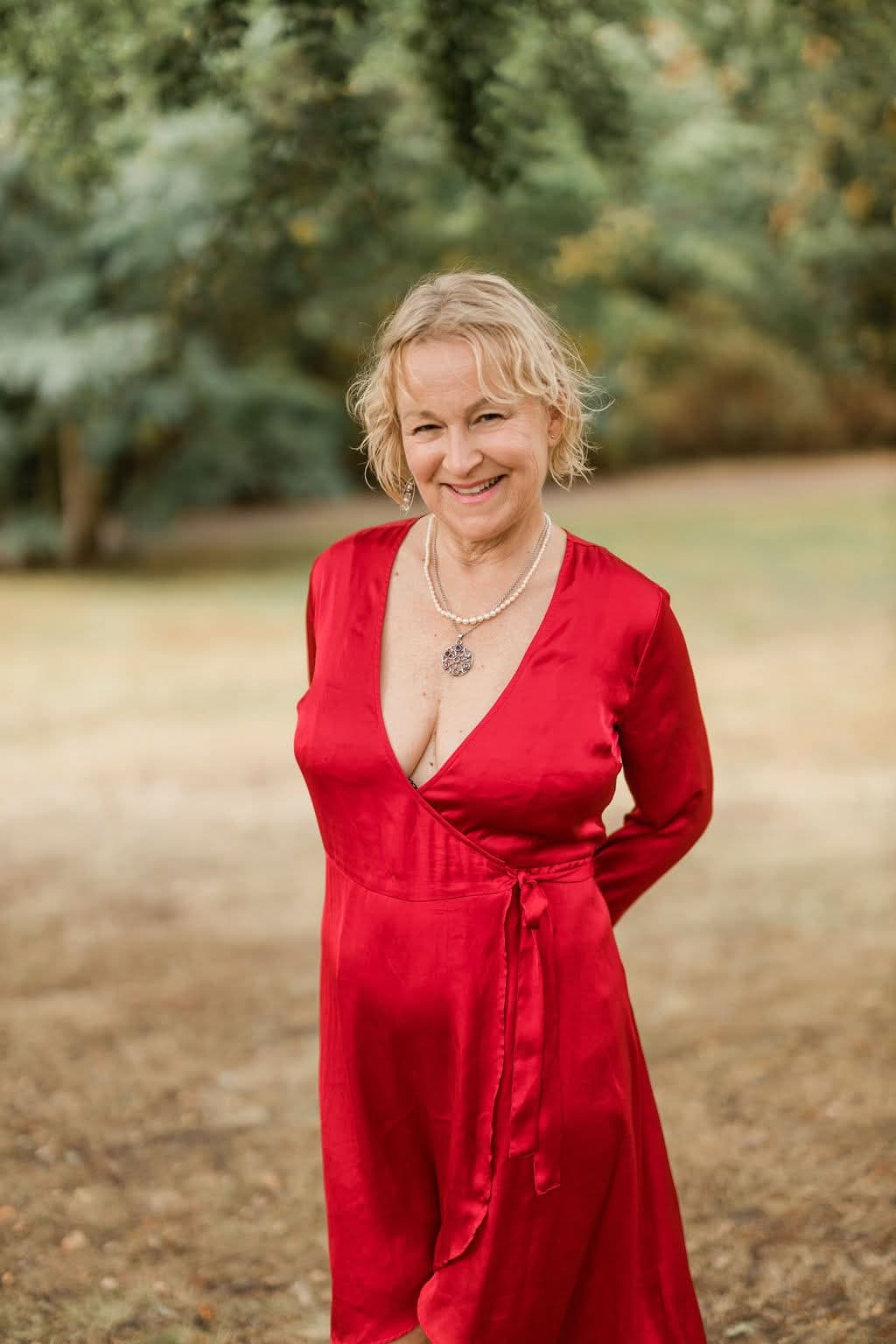 Kristina Bellman smiling in a red wrap dress among autumn trees