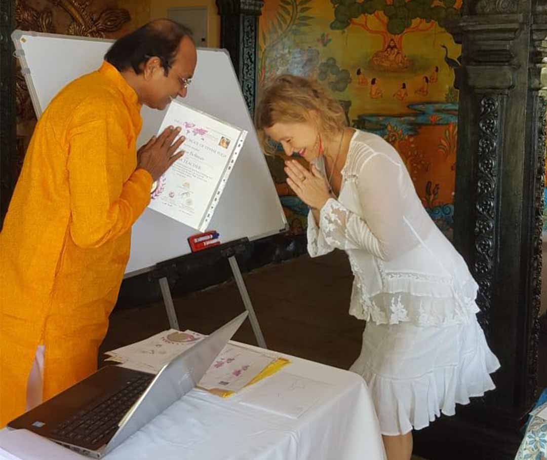 Kristina bowing with folded hands as a teacher presents her yoga certificate