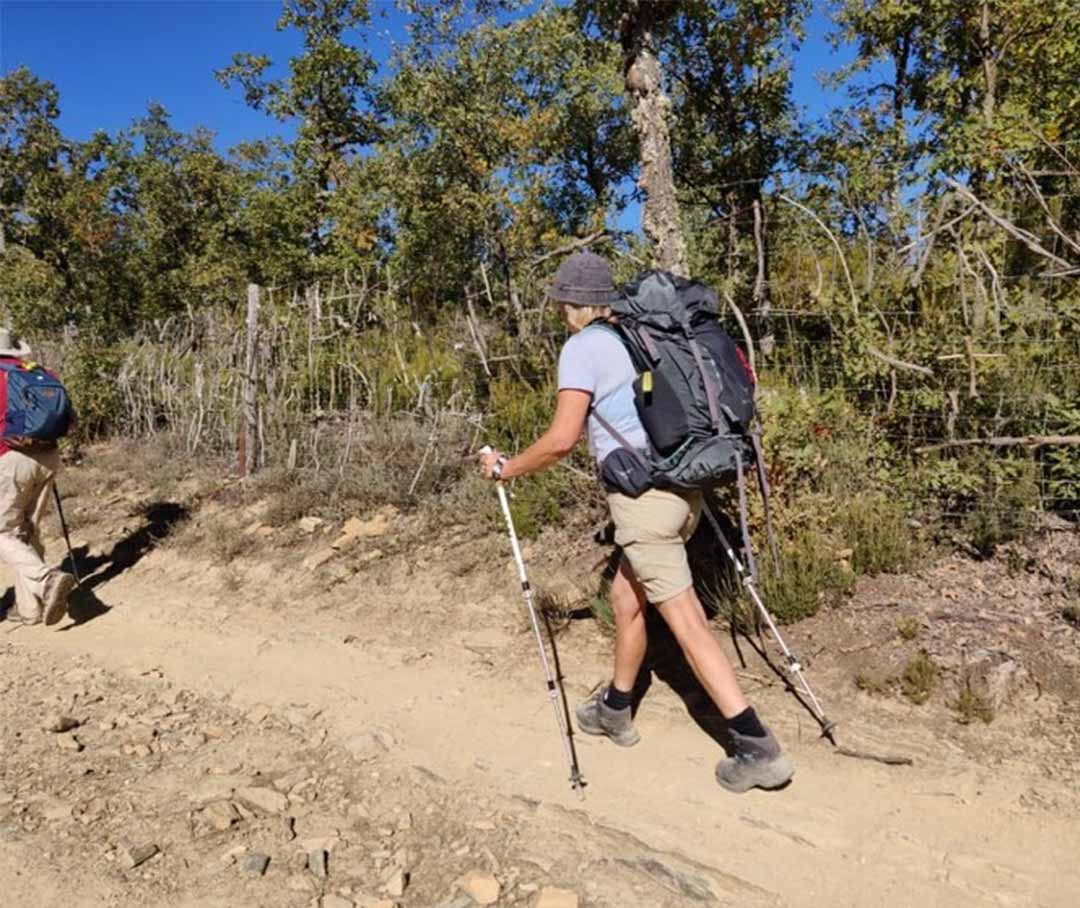 Kristina walking a dusty trail with a backpack and poles